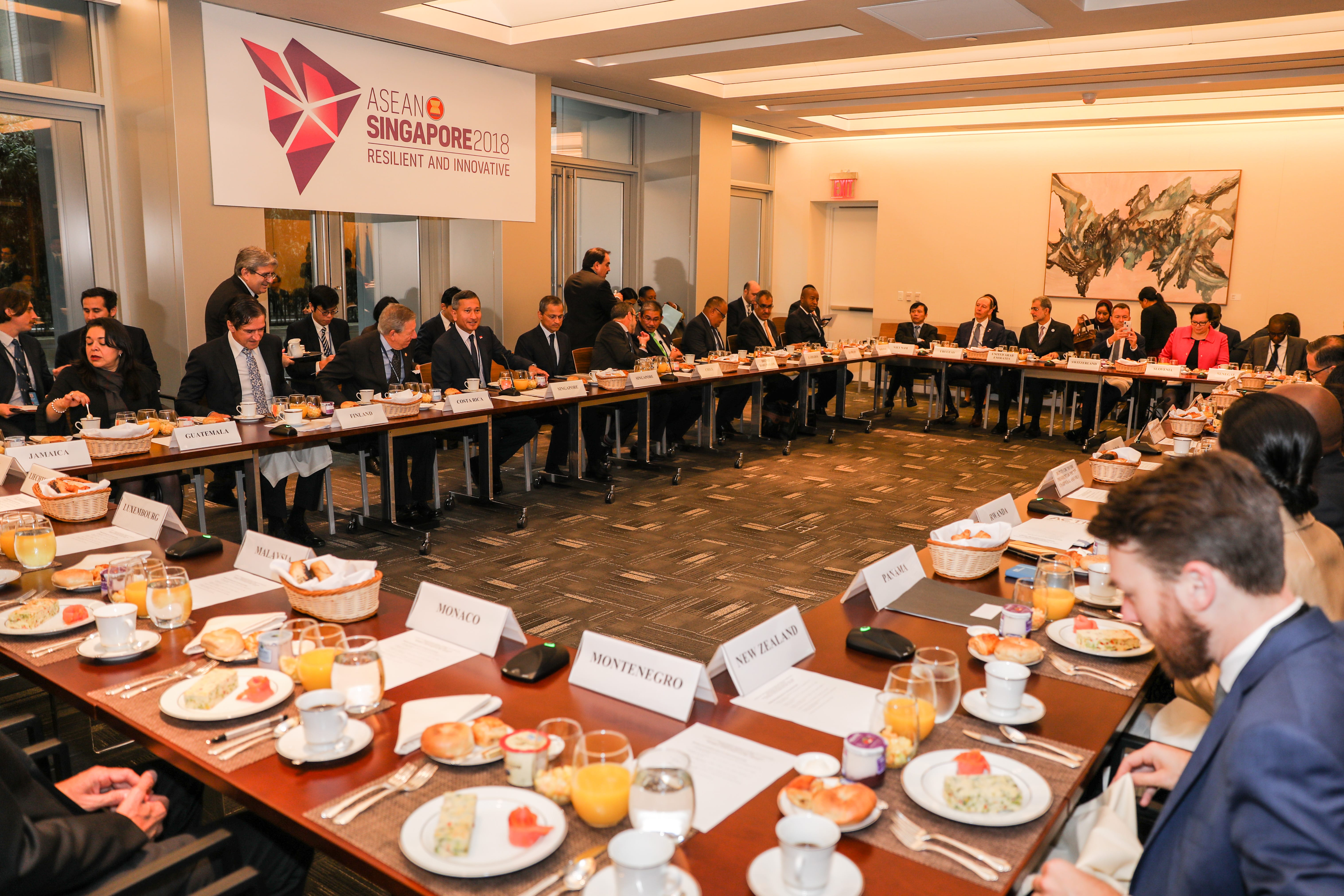 People seated at long tables with place cards at an ASEAN Singapore 2018 meeting.